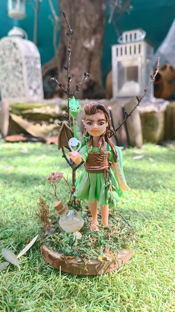 Figura de elfa con vestido verde y dragón sobre base de madera con musgo