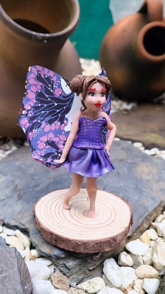 Hada con vestido morado brillante y alas de mariposa sobre base de madera