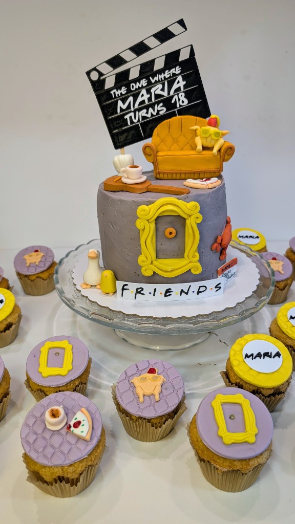 Tarta y cupcakes temática Friends con claqueta, sofá naranja y figuras en porcelana fría