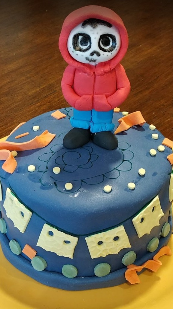 Figura de Miguel de Coco con maquillaje de calavera sobre tarta azul y papel picado